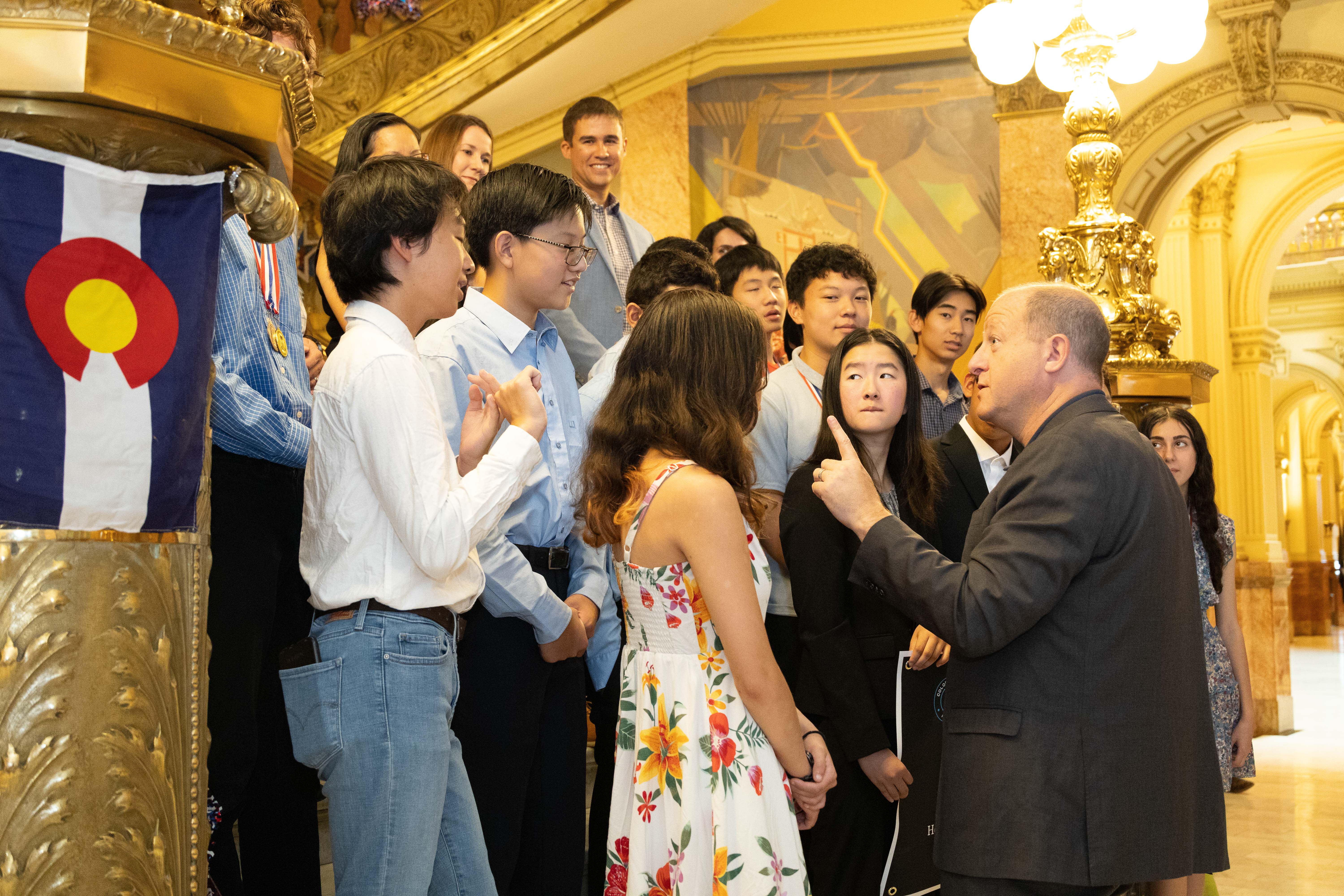 Governor Jared Polis talks with several students on the steps of the capitol rotunda. 