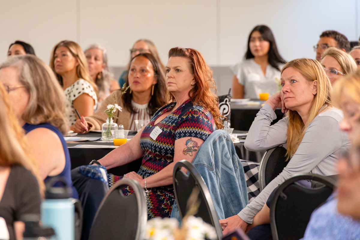 A woman sitting at a table listens to speakers talk about the importance of daily attendance.