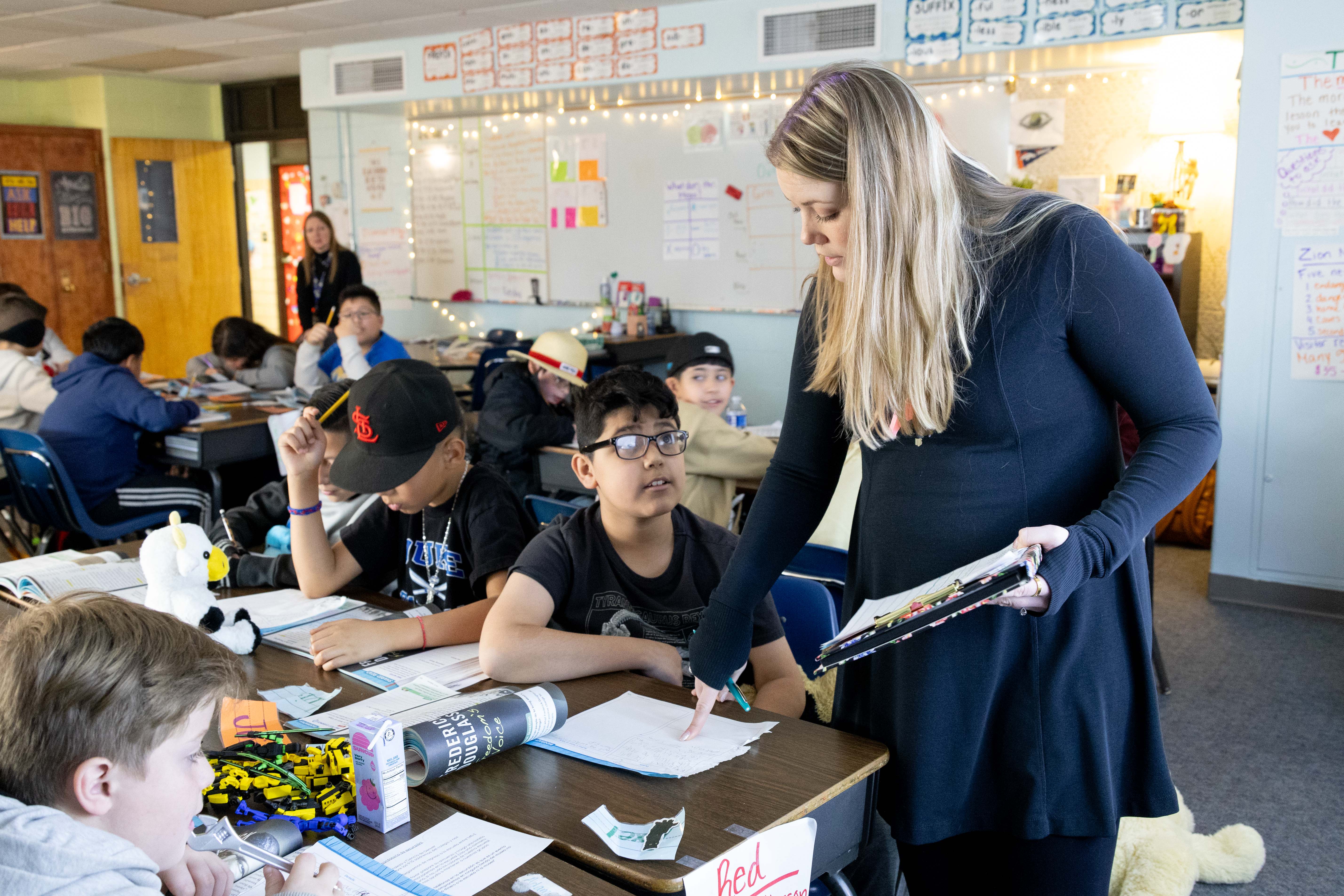 A teacher reviews a student's work at his desk. 