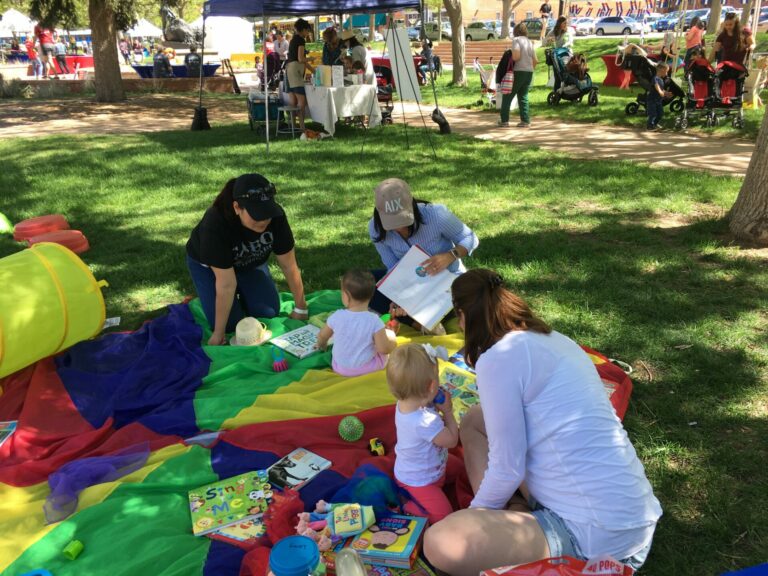 A group of families on a blanket at the park reading to young children