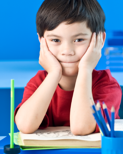 Young child smiling shyly with his chin in his hands and his elbows on a book.